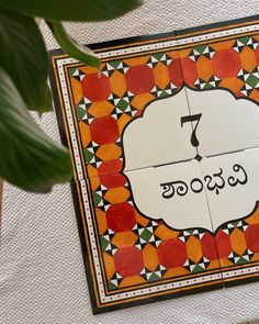 an orange and black tile with the number seven on it, in front of a potted plant