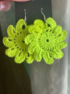 a pair of green crochet earrings hanging from a woman's hand,