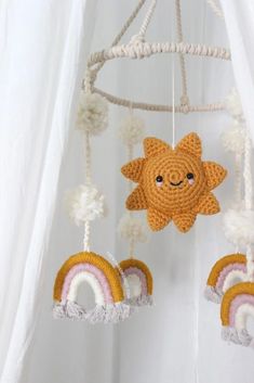 a crocheted sun and rainbow mobile hanging from a white curtain