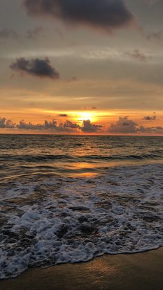 the sun is setting over the ocean with waves coming in to shore and some clouds