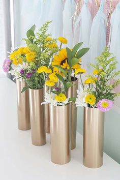 four gold vases with flowers in them sitting on a white counter next to a window