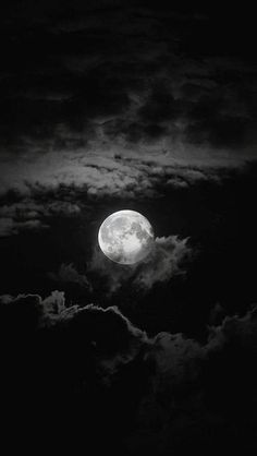 the full moon is shining brightly in the dark sky above clouds, with black and white colors