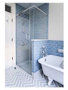 a white bath tub sitting next to a walk in shower under a bathroom window with blue tiles on the walls