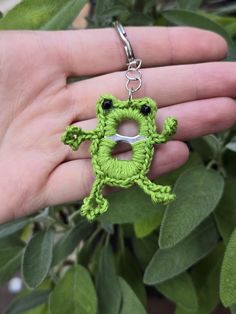 a green frog keychain is being held by someone's hand with scissors