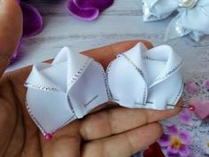 someone is holding three white bows in their hand, with flowers and beads on the table behind them