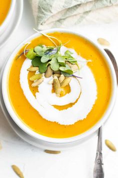 two white bowls filled with carrot soup and garnished with green leaves on top