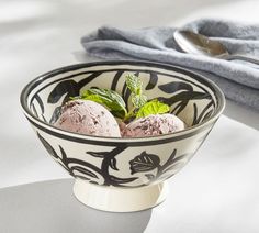 two scoops of ice cream in a black and white bowl with leaves on it