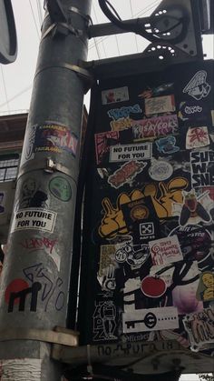 a street sign covered in lots of stickers next to a pole with a traffic light