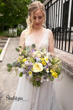 a woman in a white dress holding a bouquet of yellow and purple flowers on her wedding day