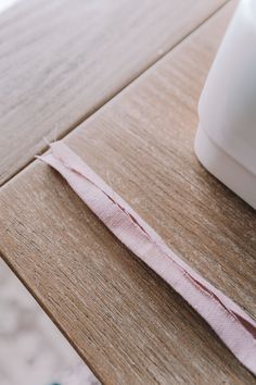 a piece of pink ribbon sitting on top of a wooden table next to a white container