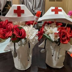 two white vases with red crosses and flowers in them sitting on a wooden table