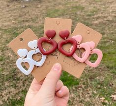 three heart shaped earrings are being held in front of a tag with the word love on it