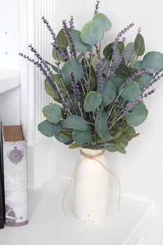 a white vase filled with purple flowers on top of a shelf next to a book