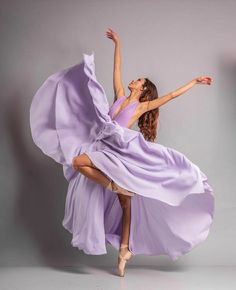 a woman in a purple dress is dancing with her arms spread out and legs bent