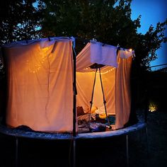 an outdoor tent is lit up at night with lights on the top and curtains around it