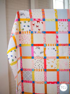 a colorful quilt hanging from the side of a white brick wall next to a window