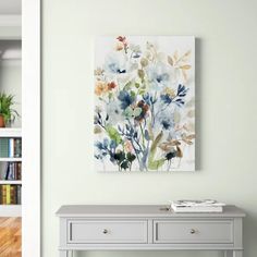 a painting is hanging on the wall above a gray console table with bookshelves in the background