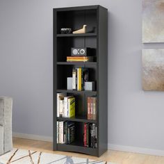 a black bookcase in a living room next to a gray chair and white rug