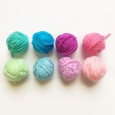 four balls of yarn are lined up in different colors on a white surface, one is pink, the other is blue