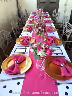 the table is set with pink napkins and gold place settings, along with silverware