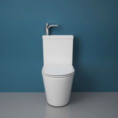 a white toilet sitting on top of a gray floor next to a blue wall with a silver faucet