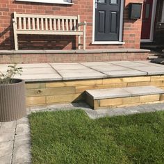 a wooden bench sitting on the side of a brick building next to a grass covered yard