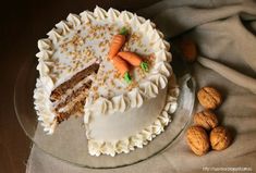 a carrot cake with white frosting and walnuts next to it on a glass plate