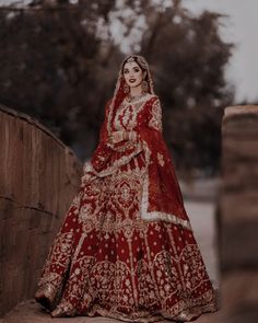 a woman in a red and gold bridal gown standing on a brick wall with trees in the background