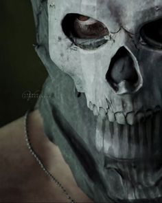 a man wearing a skull mask with chains around his neck and eyes, in front of a dark background