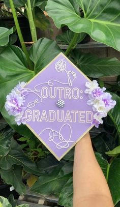 someone holding up a purple graduation cap that says, outro graduated with flowers on it