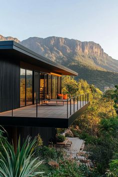 a house with mountains in the background and wooden decking on the outside, surrounded by greenery