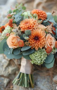 a bridal bouquet with orange flowers and greenery on the side of a rock