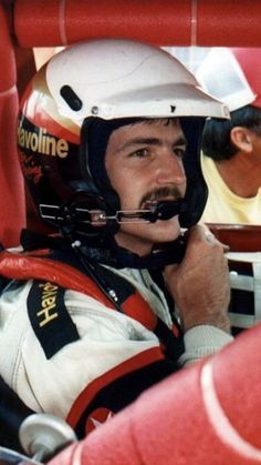 a man sitting in the drivers seat of a race car wearing a helmet and goggles