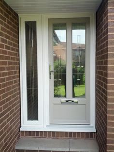 a white door and window on a brick building with grass in the front yard behind it