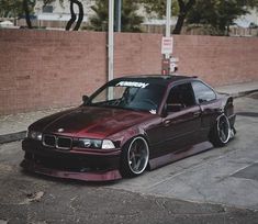 a maroon car parked on the side of a street next to a brick wall and trees