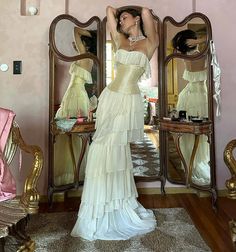 a woman standing in front of a mirror wearing a white dress with ruffles