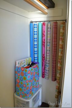 an organized closet with colorful wrapping paper and storage bins on the bottom shelf in front of it