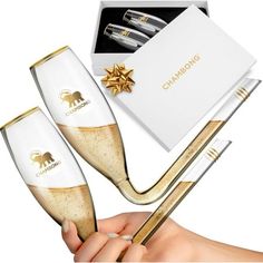 two champagne flutes with gold rims in a gift box and one holding a straw