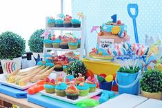 a table topped with cupcakes and cakes covered in frosting next to potted plants