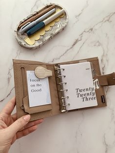 a hand holding an open book with writing on it and a pen in the middle