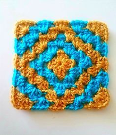 a crocheted square with an orange and blue design on the center is sitting on a white surface