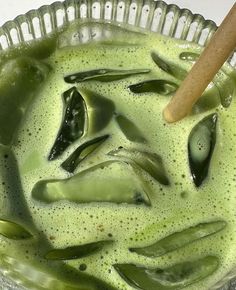 a glass bowl filled with green liquid and a wooden spoon in the bottom right corner