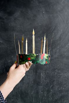 a person holding up a paper crown with candles on it and holly leaves in the middle