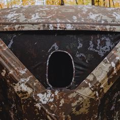 an old rusted out car with a hole in the side window and trees in the background