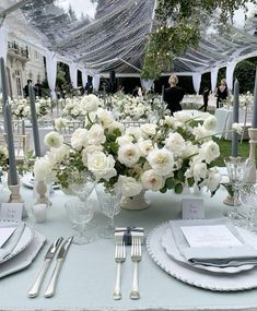 the table is set with white flowers and silverware