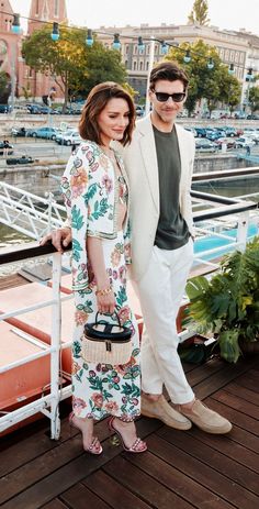 a man and woman standing next to each other on a deck near water with boats in the background