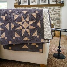 a bed with a quilt on top of it next to a table and chair in front of a brick wall