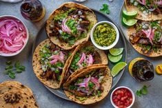 several tacos and salsas on a plate with condiments, lime wedges, cilantro, and red onions