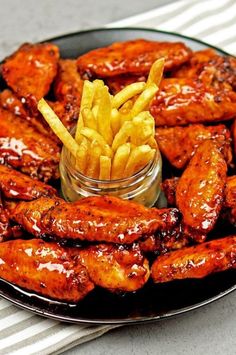 a black plate topped with chicken wings and french fries