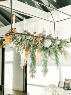 a chandelier with candles and greenery hanging from it's ceiling in a dining room